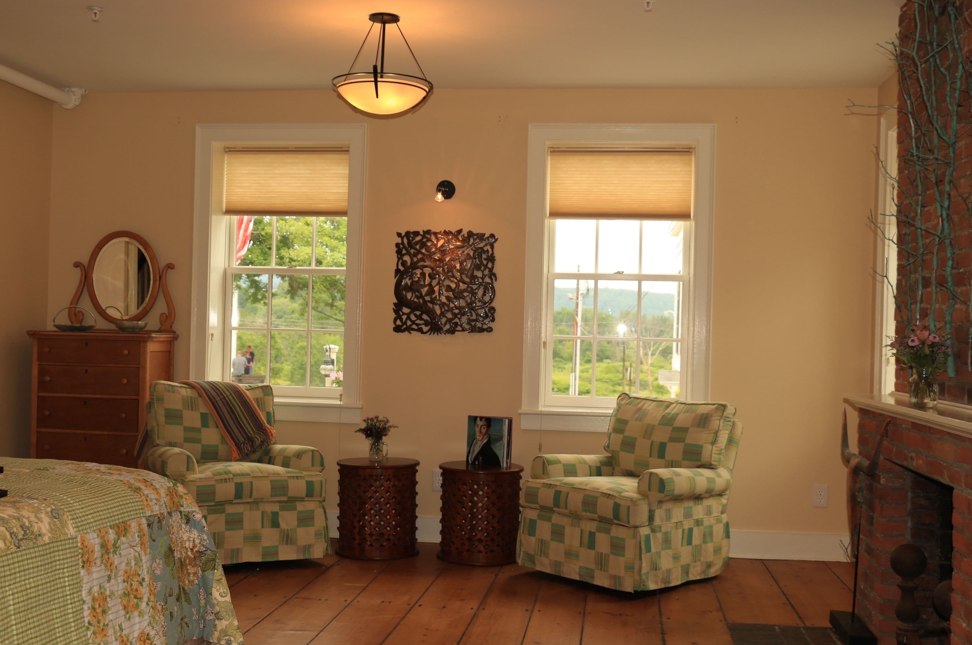 A cozy room with a bed, two armchairs, a dresser, and a fireplace.