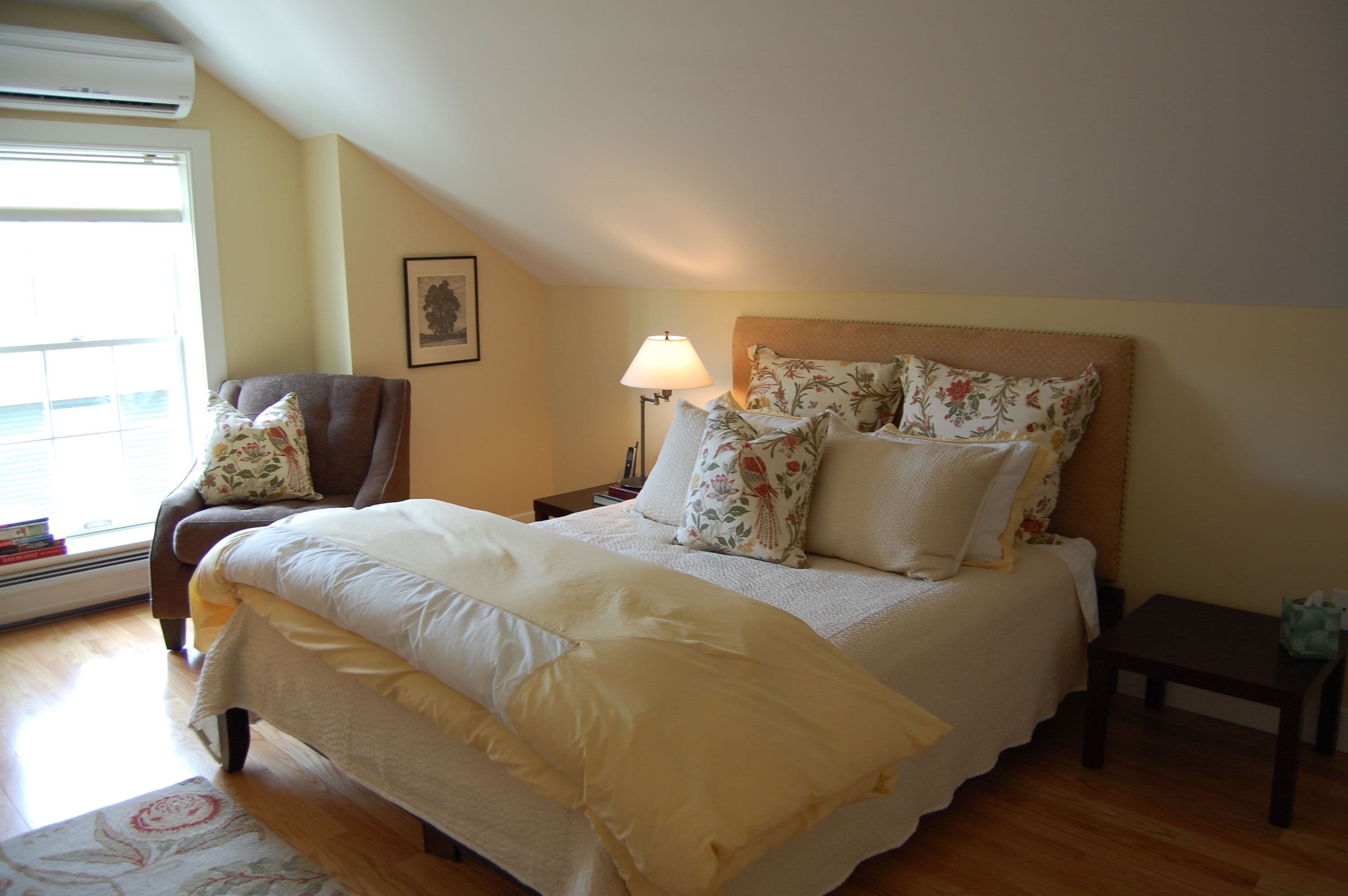 Un dormitorio ordenado con cama, una silla, una mesita de noche y una lámpara.