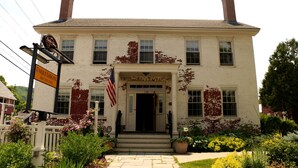 A two-story building with a white facade and red brick accents, featuring a front entrance with steps and a flag. - Butler House (Stowe)