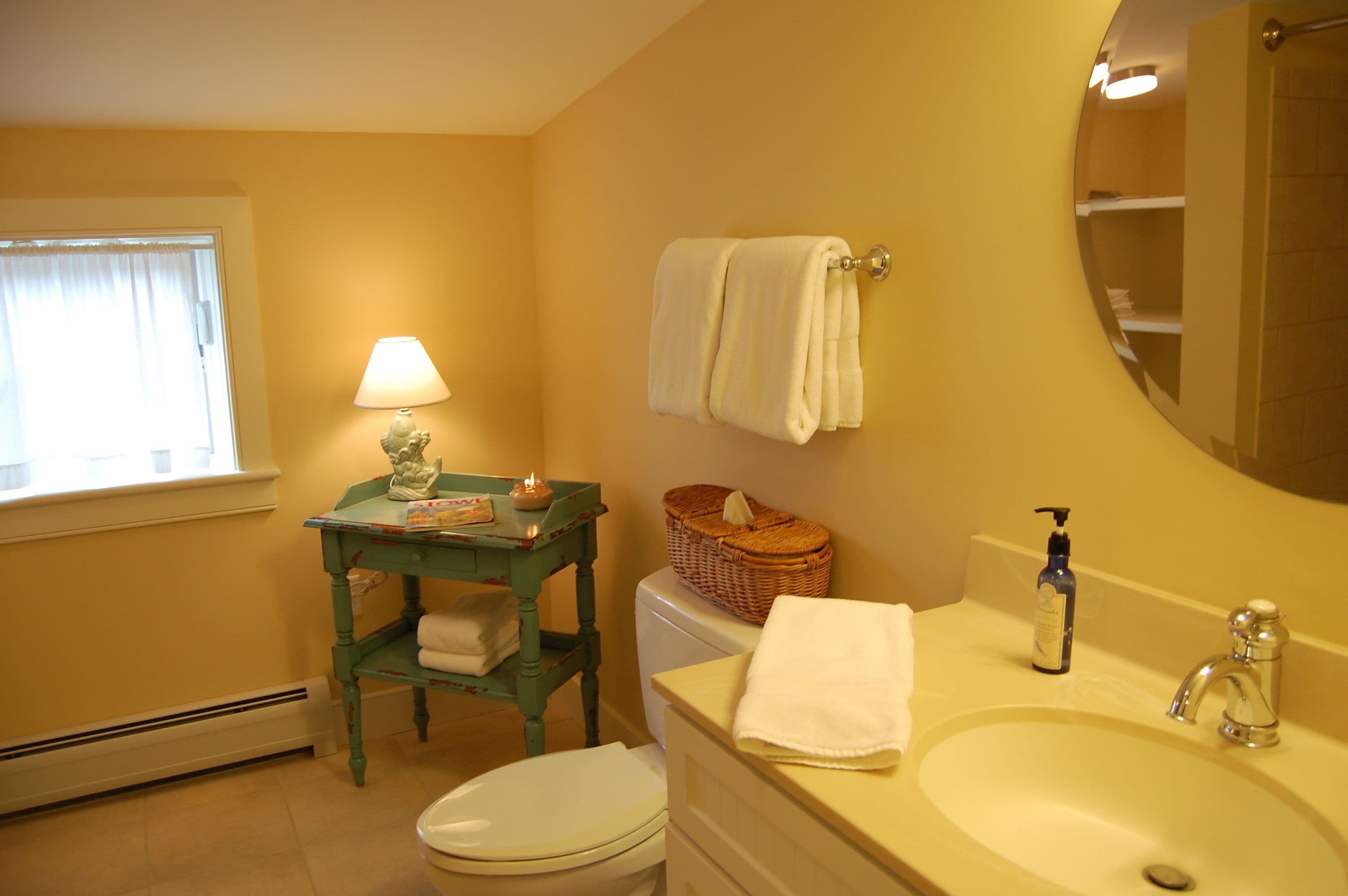 A bathroom with a toilet, sink, and a table with a lamp and basket.