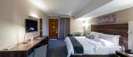 Habitación de hotel con cama, escritorio, televisor y una obra de arte colgada en la pared.