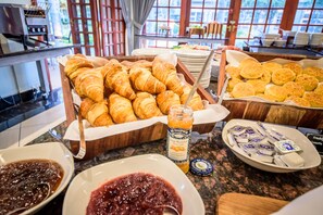 Un bufé con croissants, galletas, mermeladas y un tarro de confitura.