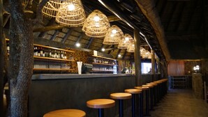 Zona de bar con taburetes de madera, barra y lámparas de mimbre colgantes.