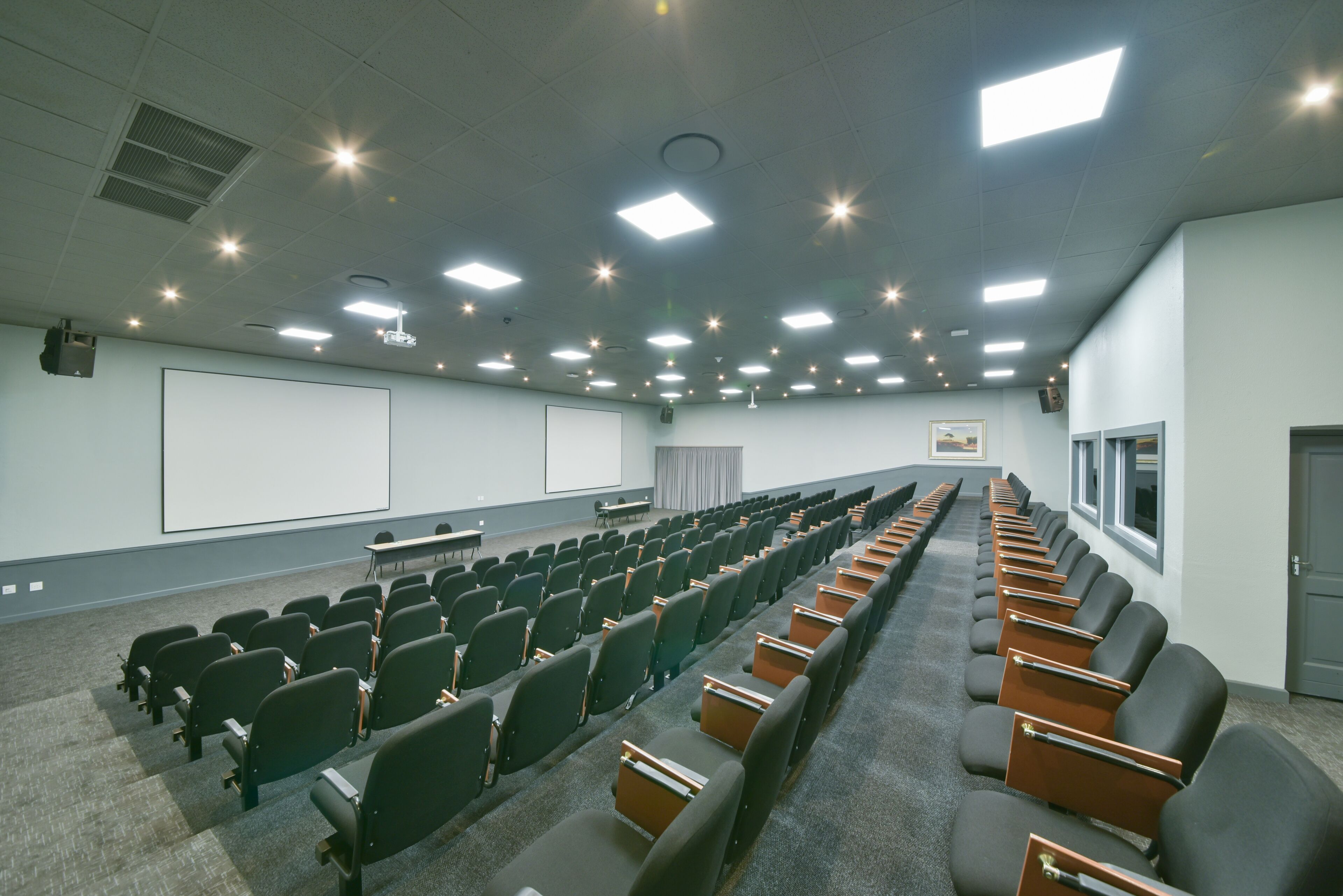 Konferenssihuone, jossa on riveissä tuoleja, projektorikangas ja suuri kirjoitustaulu.