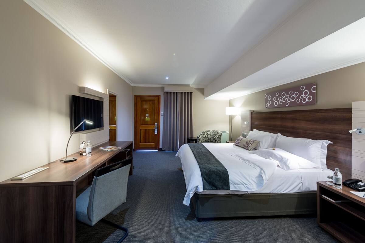 Habitación de hotel con cama, escritorio, silla, televisor y una pared con diseño circular.