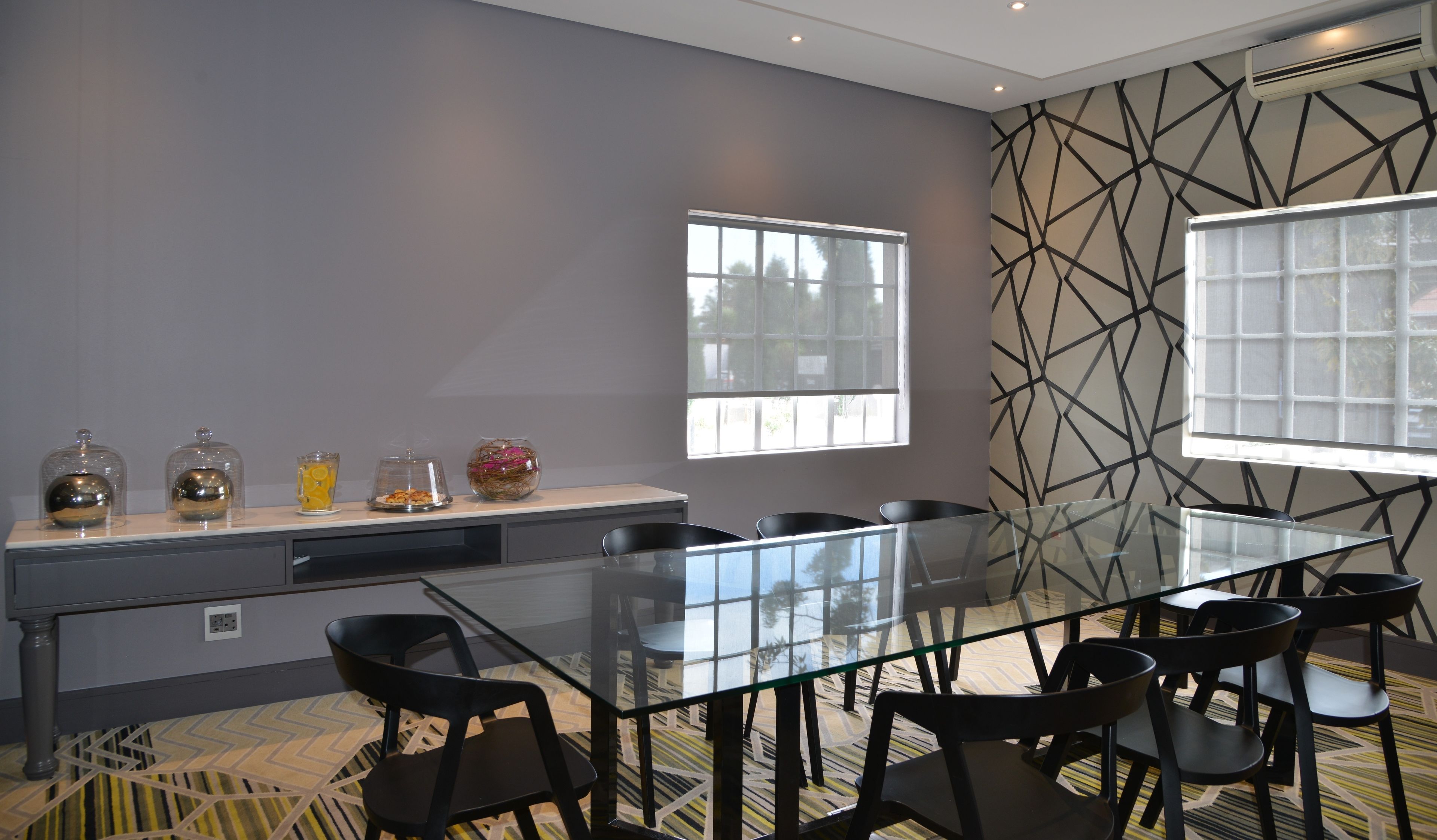 Una sala de reuniones moderna con una mesa de vidrio, sillas negras y una pared con diseño.