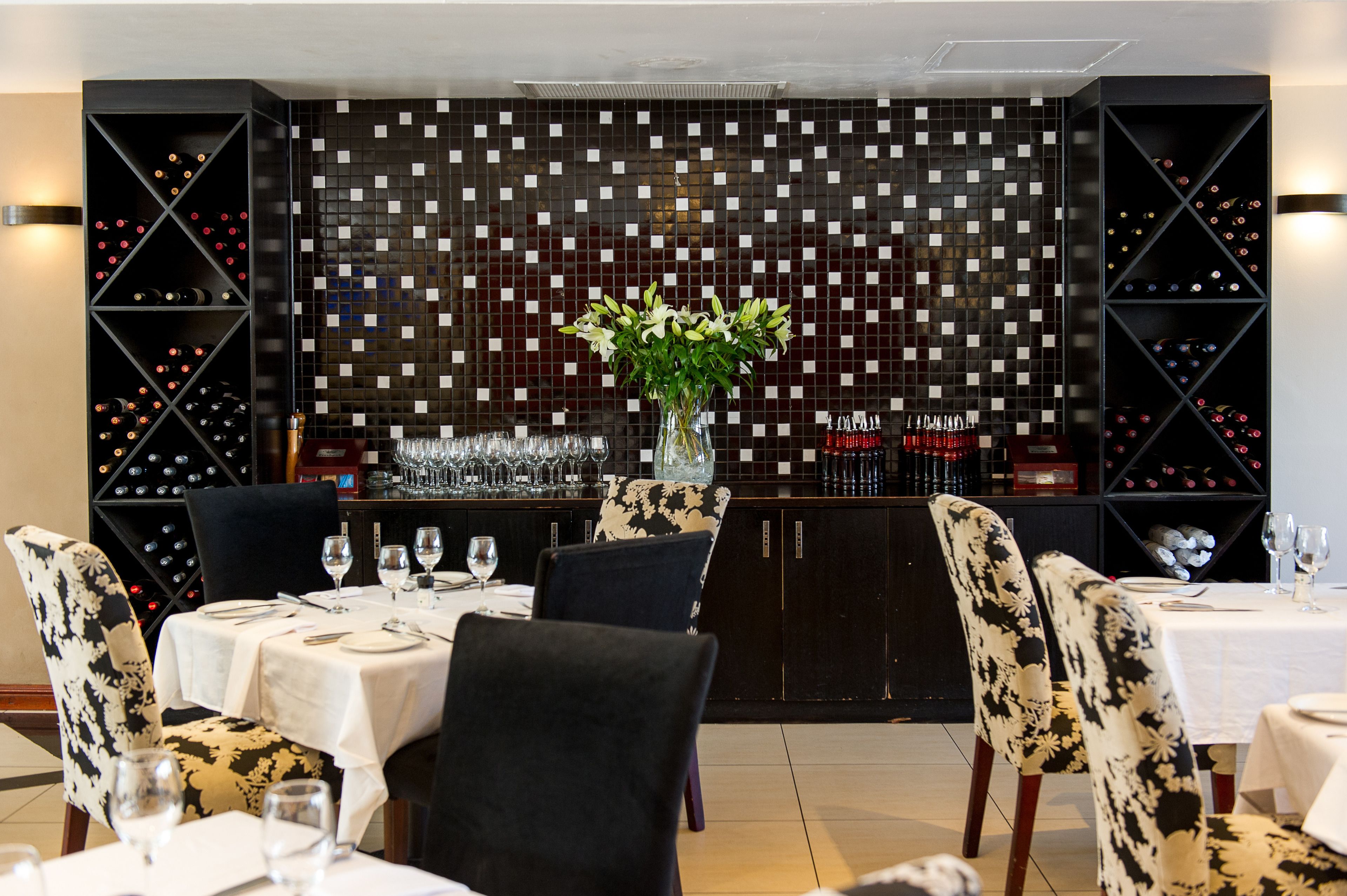 Un restaurante con una pared de baldosas blanco y negro, una estantería para vinos y una mesa dispuesta para comer.