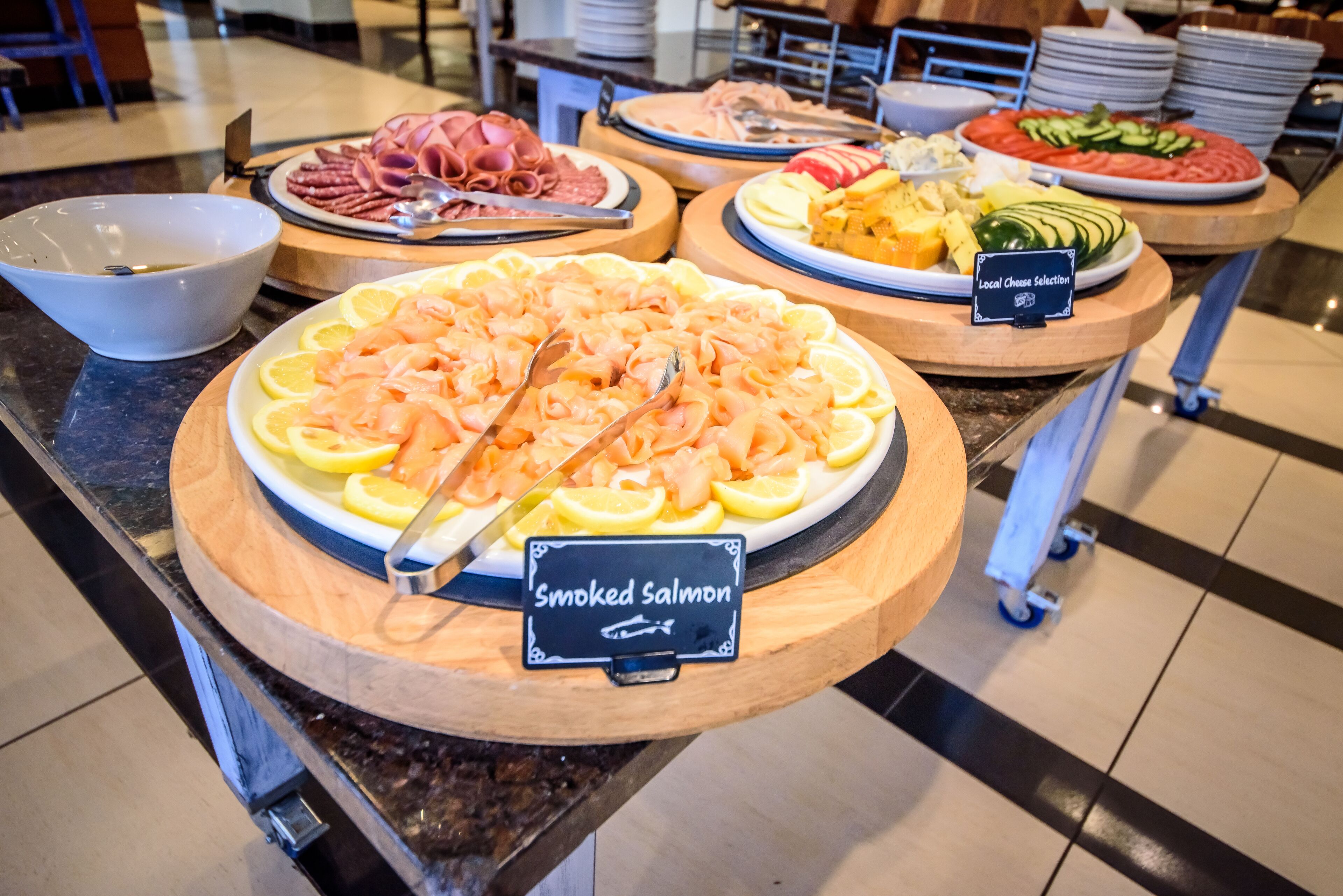 Buffet com diversas opções de comida, incluindo salmão defumado, presunto e saladas.