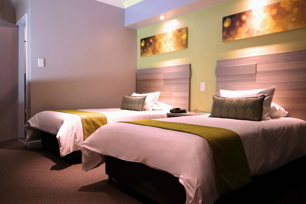 Una habitación de hotel con dos camas, cada una con cabecera, mesita de noche y lámpara.