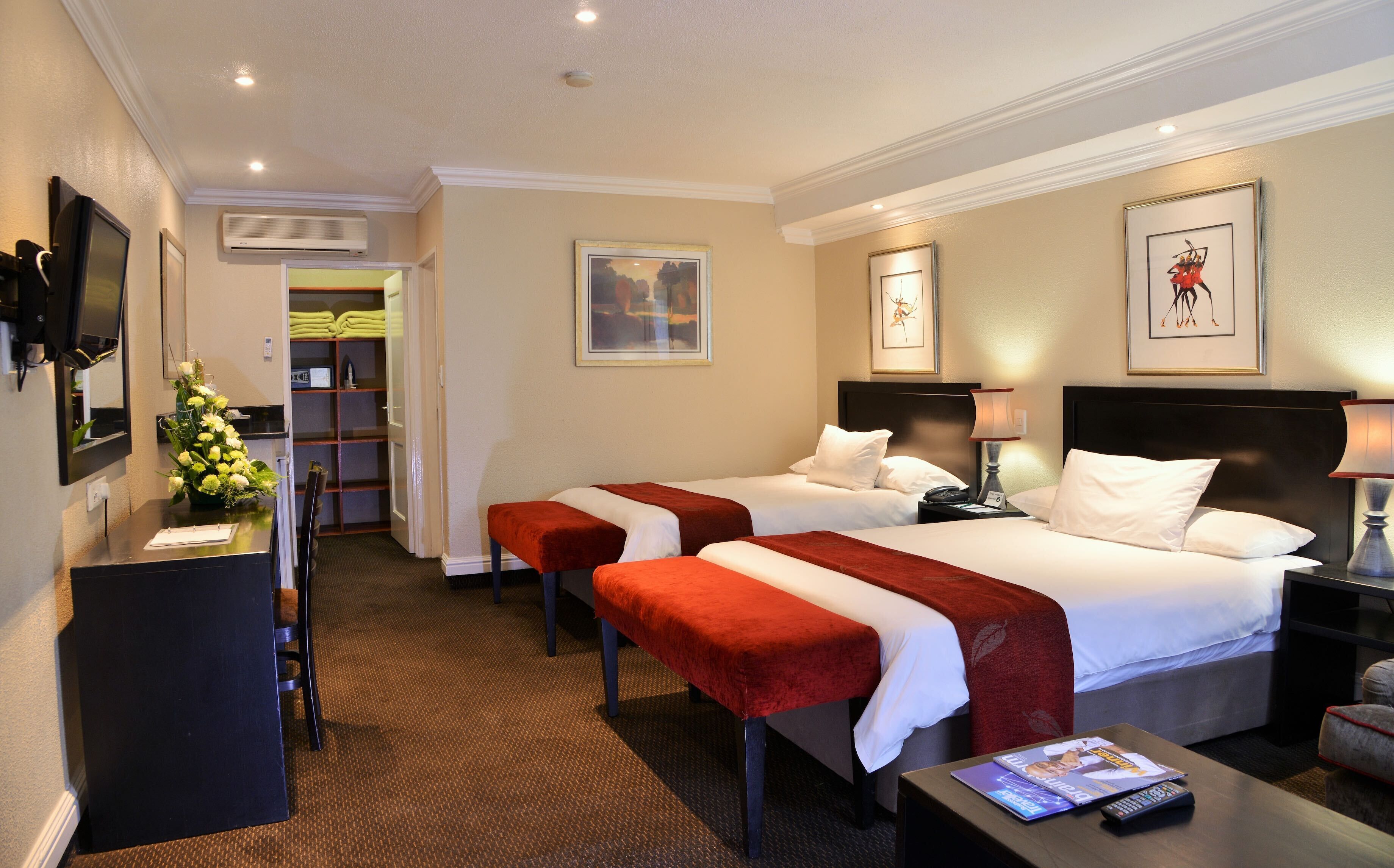 A hotel room with two beds, a desk, a chair, a TV, and a bathroom with a shower and toilet.