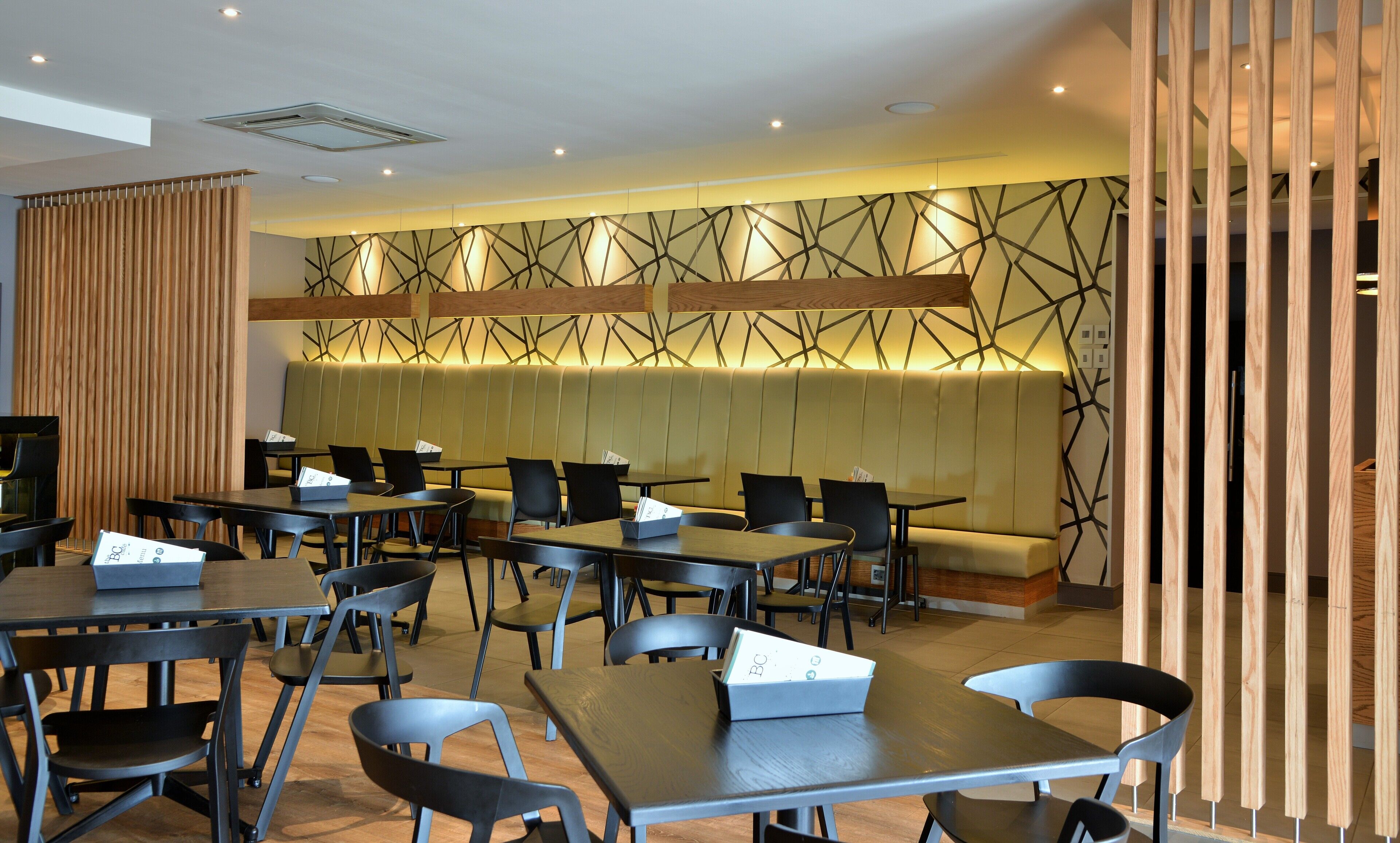 A modern dining area with multiple tables and chairs, a central seating area with a cushioned bench, and a geometric patterned wall.