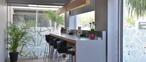 A modern kitchen with a bar area, large windows, and potted plants.
