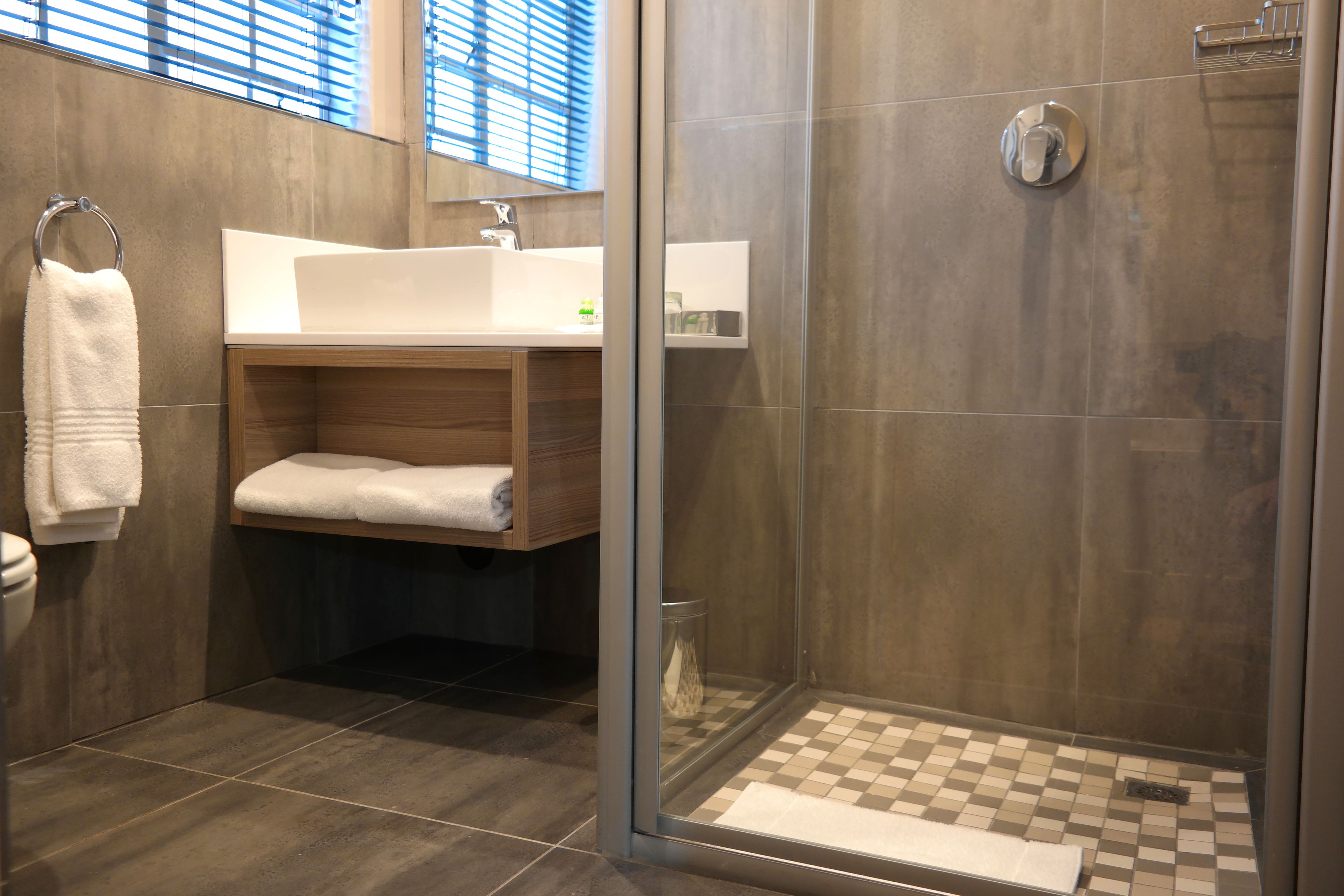 Un bagno moderno con doccia vetrata, un mobile bagno in legno con lavandino bianco e un porta asciugamani.