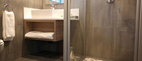 Un bagno moderno con doccia vetrata, un mobile bagno in legno con lavandino bianco e un porta asciugamani.