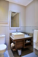 A bathroom with a white sink, mirror, and toilet. There is a towel rack and a trash can.