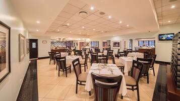 A restaurant with multiple tables and chairs, a tiled floor, and a ceiling with recessed lighting.