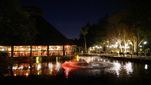 Vista nocturna de un restaurante con una fuente en primer plano.