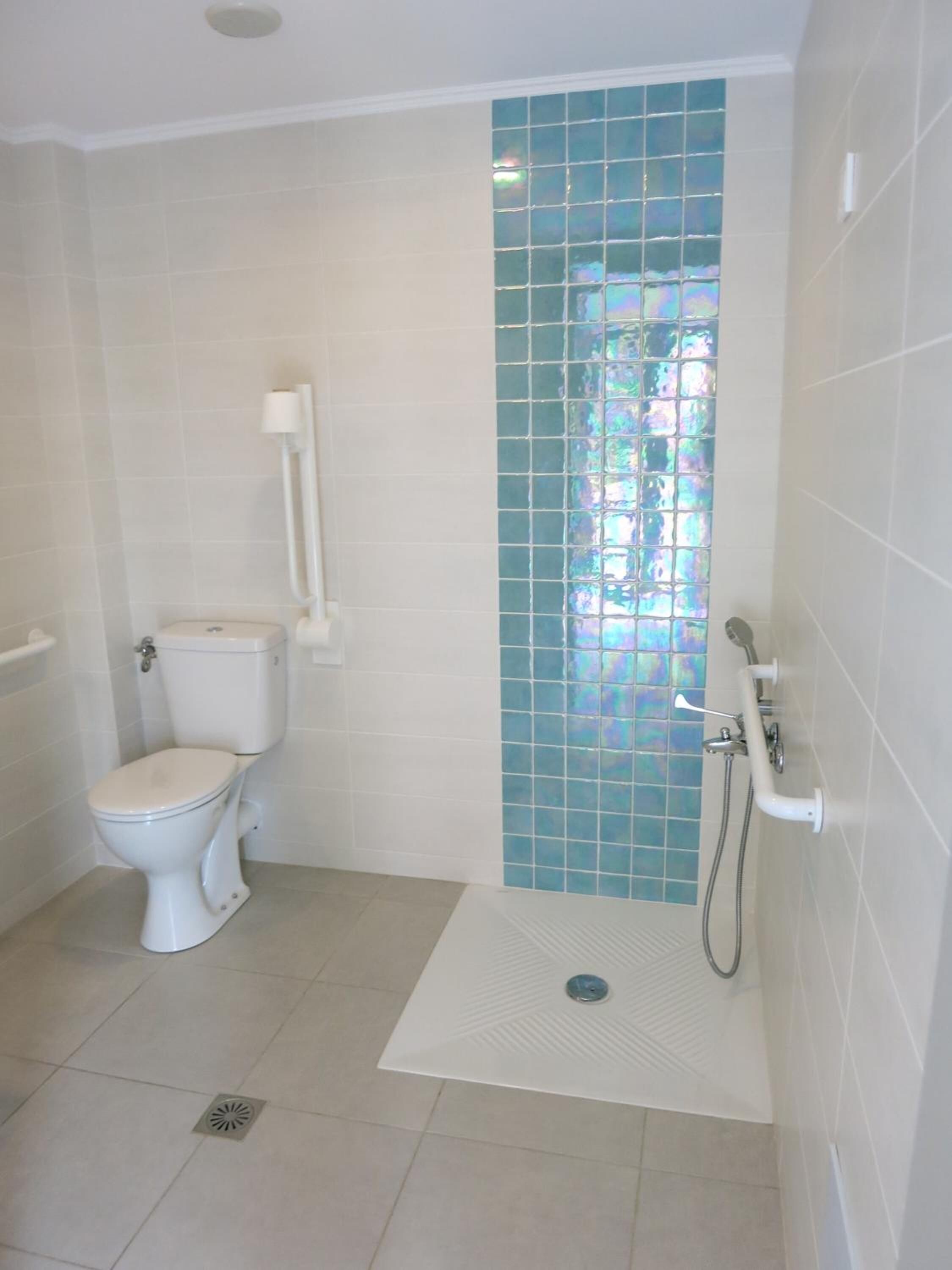 A small, clean bathroom with a toilet, a shower, and a window with blue-tinted glass.