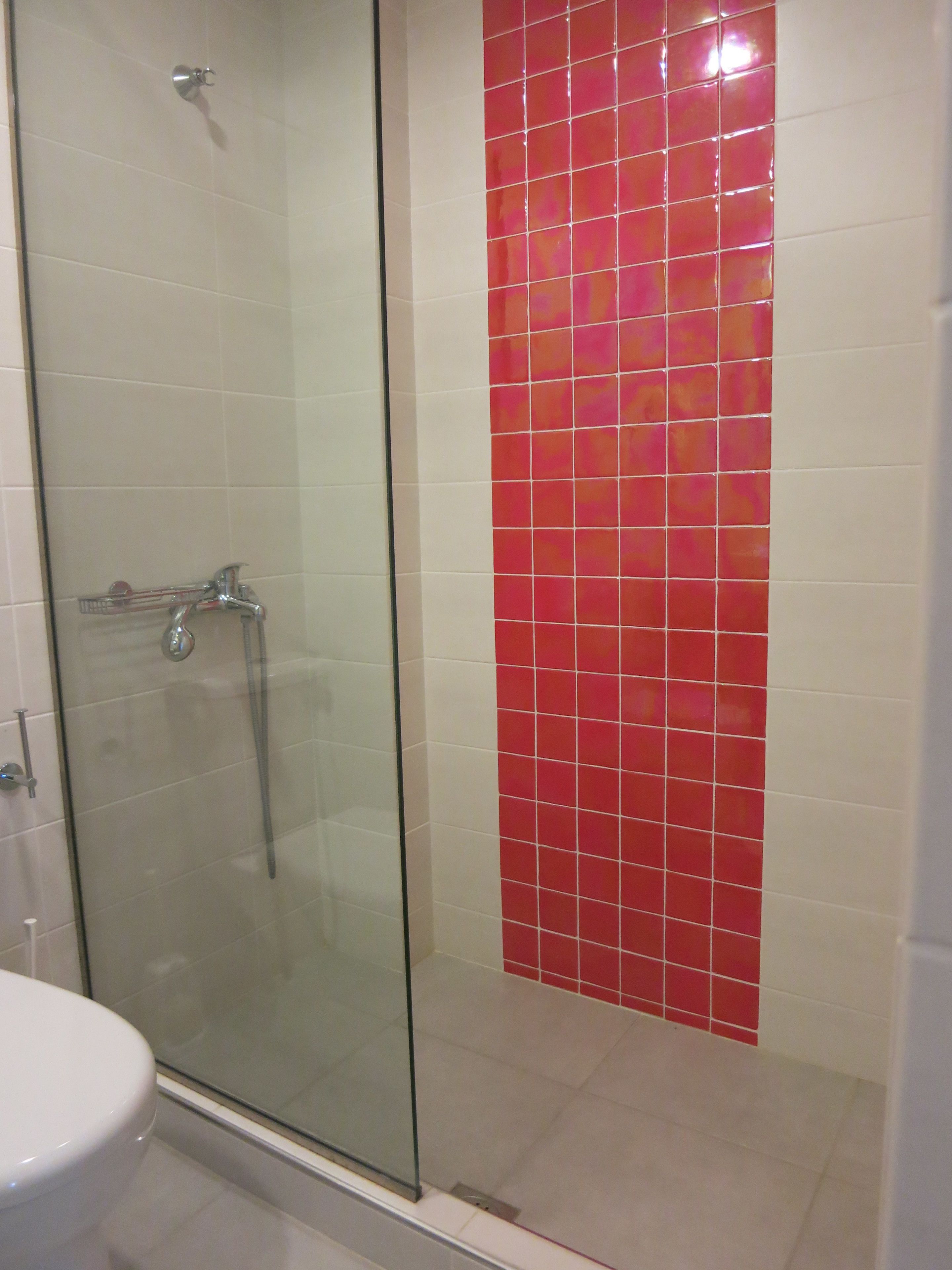 Een badkamer met een douchecabine van glas, een wit toilet en een rode betegelde muur.