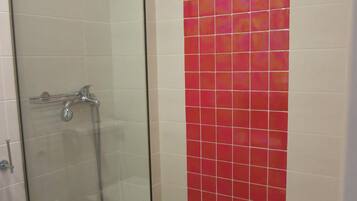 Een badkamer met een douchecabine van glas, een wit toilet en een rode betegelde muur.