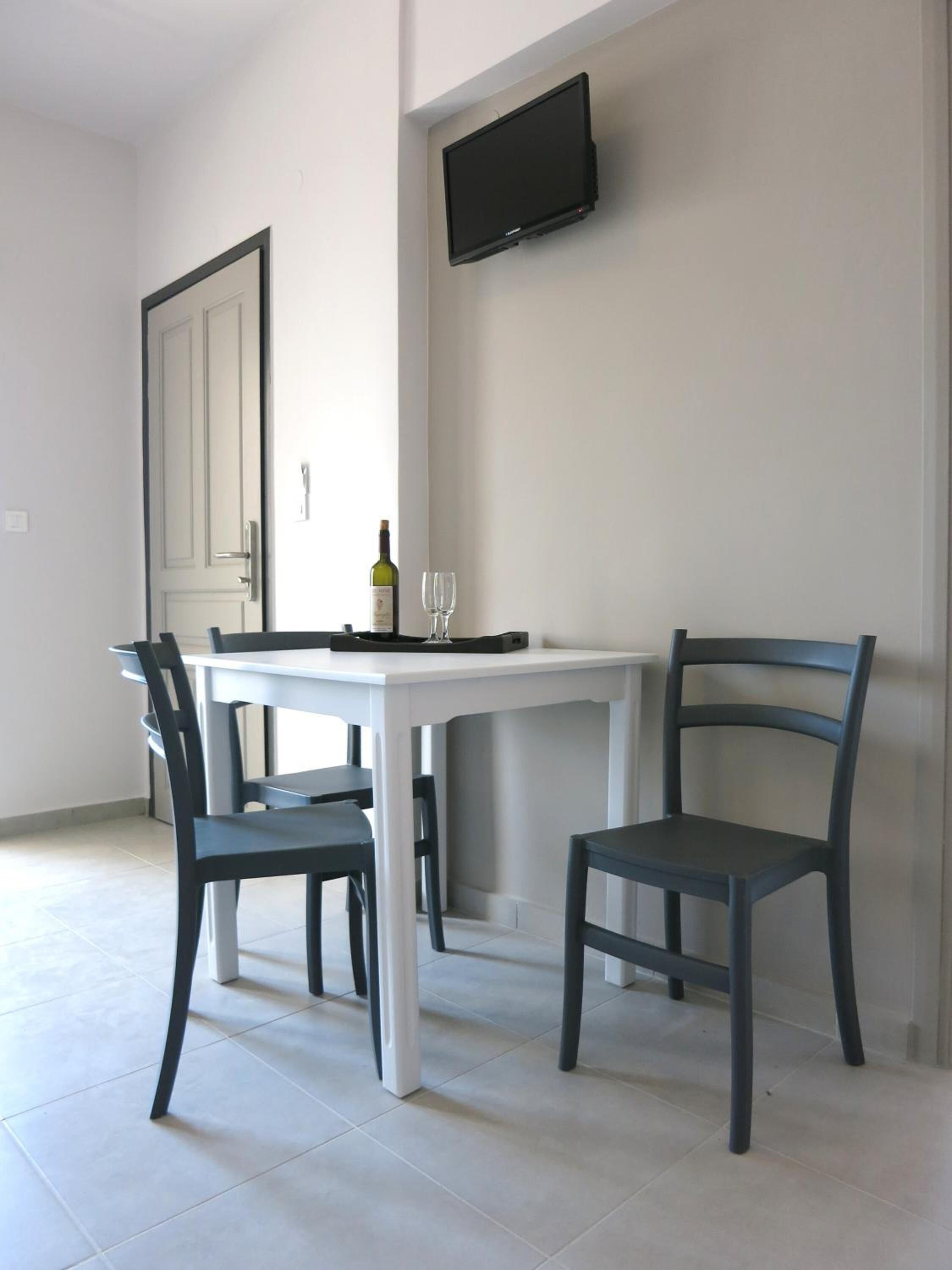 Un coin repas avec une table blanche, deux chaises, une bouteille de vin et un verre à vin.