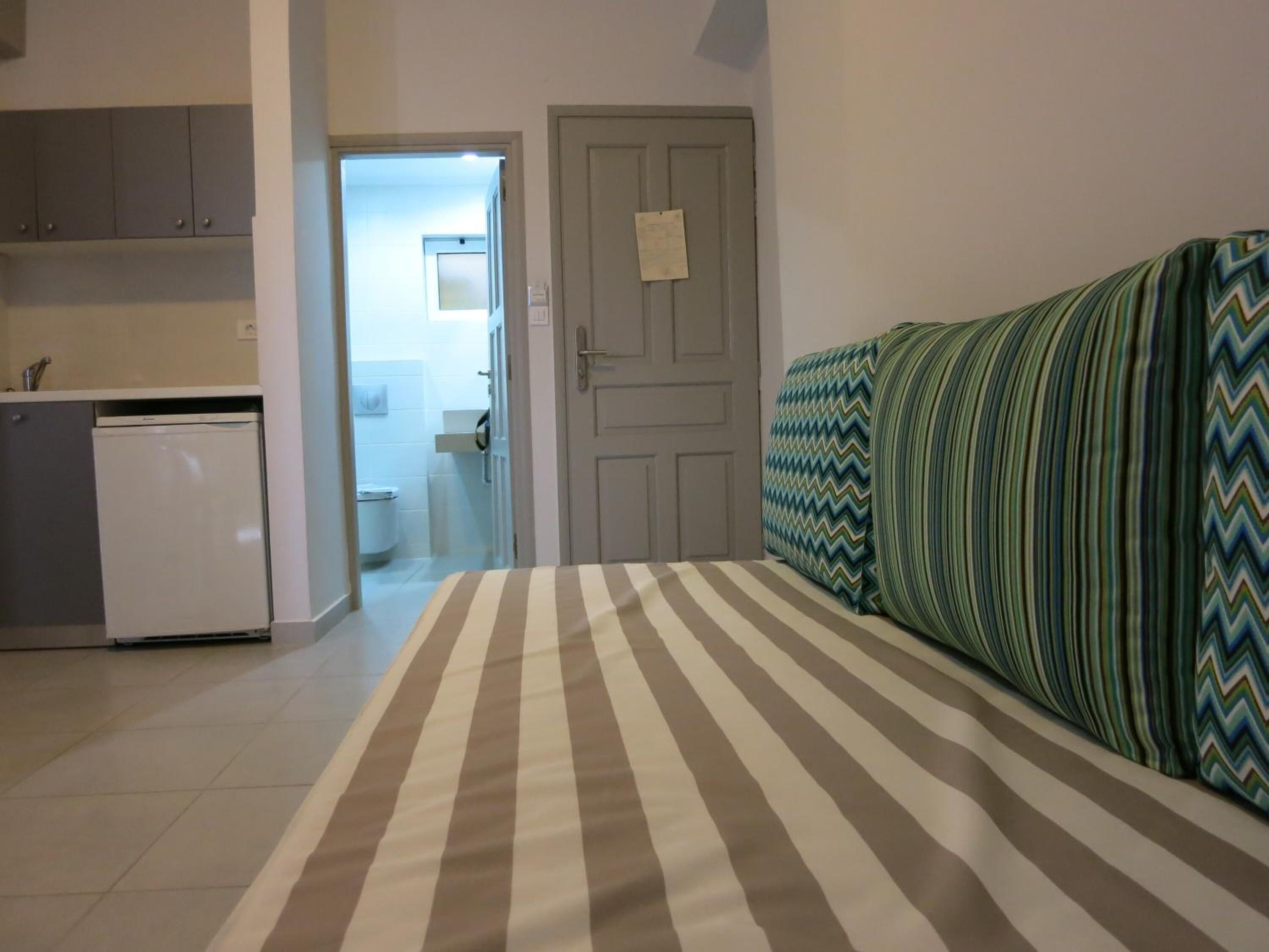 A bedroom with a bed, a sofa, a kitchenette, and a bathroom visible through an open door.
