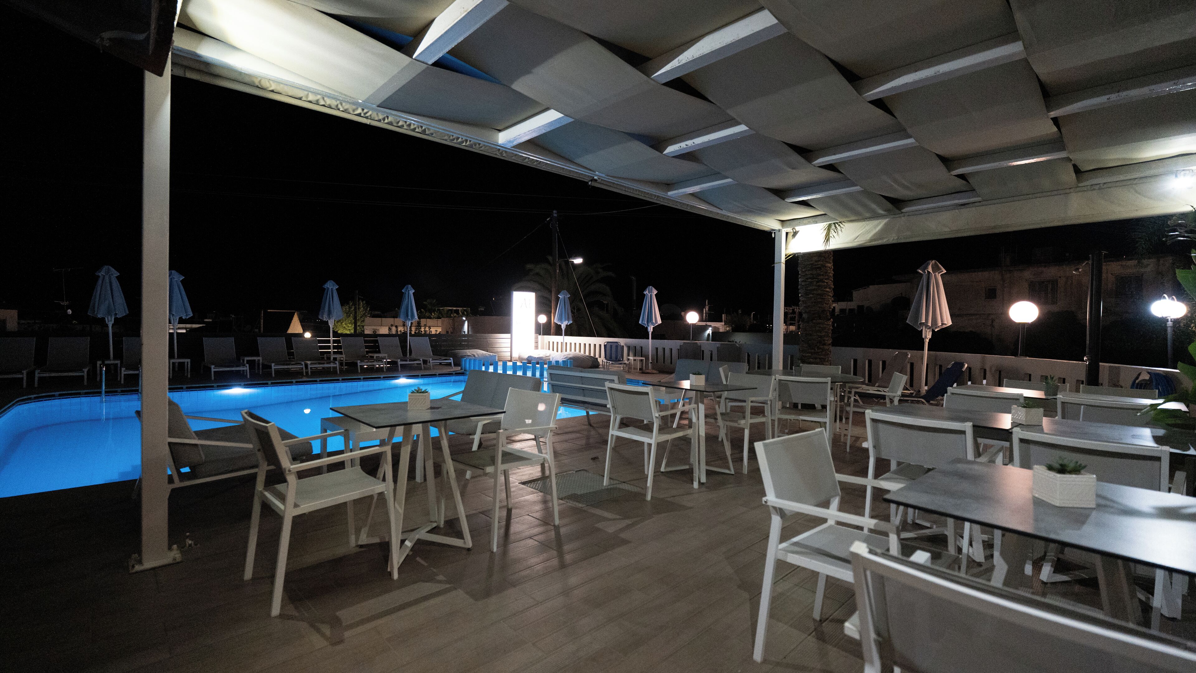 Un espace aménagé au bord de la piscine, avec des chaises longues et des tables, une piscine et des parasols.