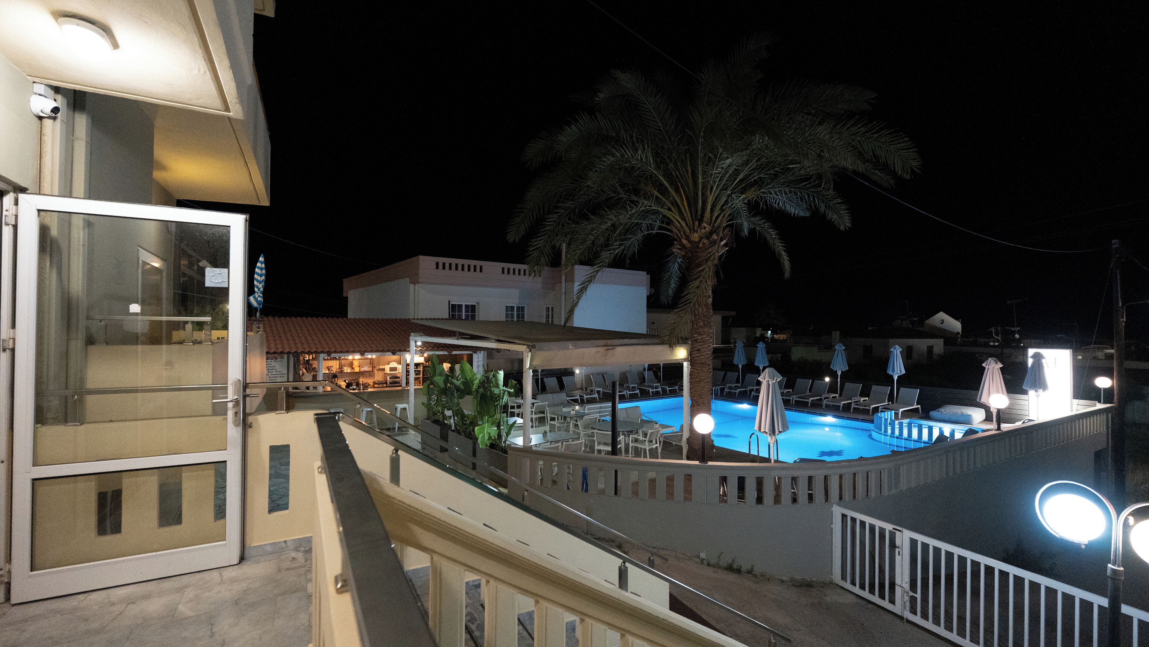 A nighttime view of a hotel with a swimming pool, lounge chairs, and palm trees.