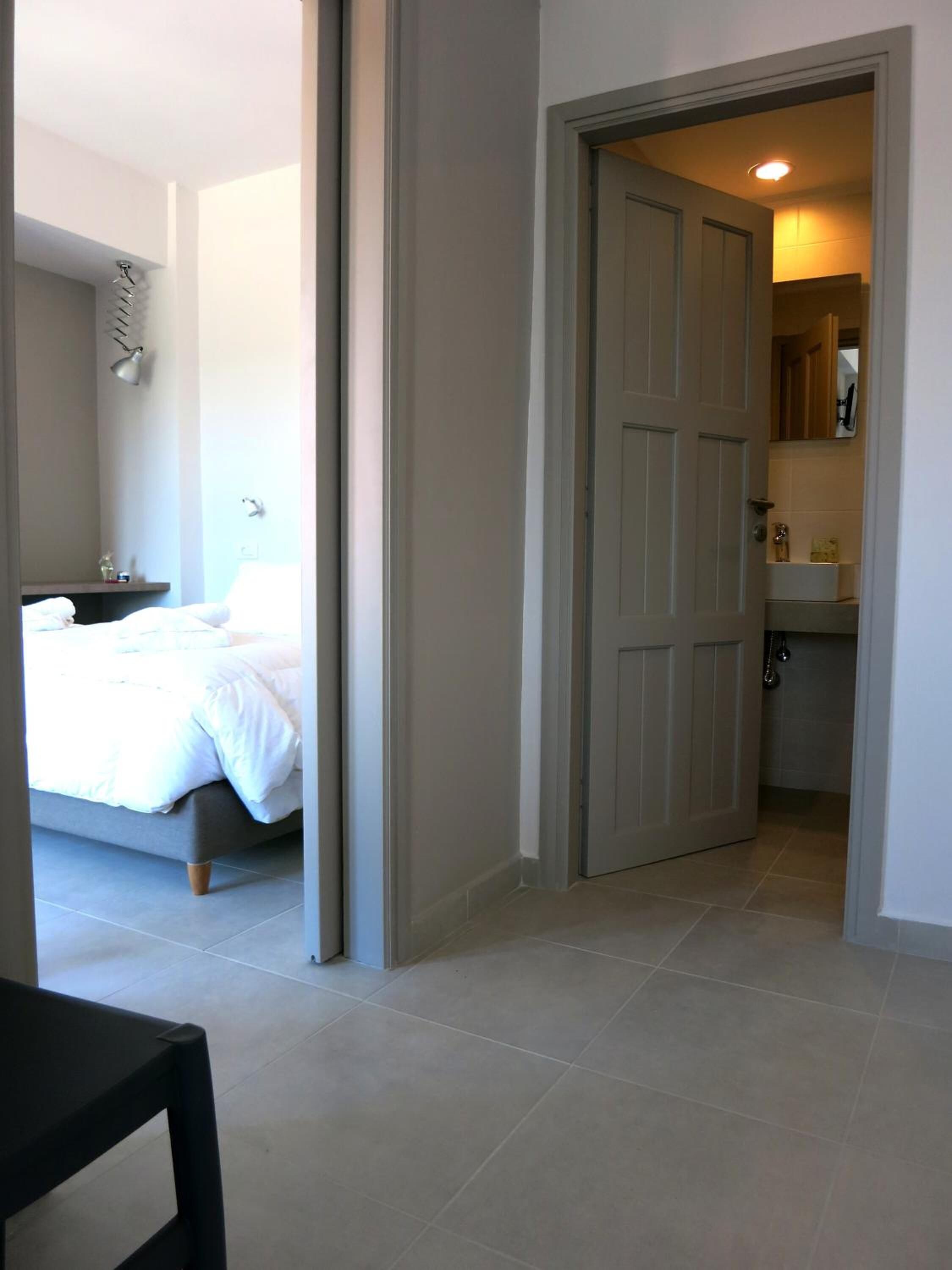 Een hotelkamer met een bed, een nachtkastje en een badkamer zichtbaar door een geopende deur.