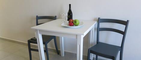 A white table with two black chairs, a bottle, and a plate with apples and grapes.
