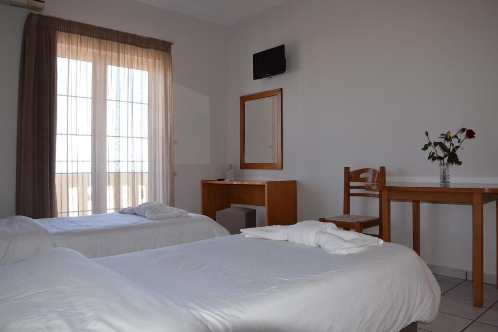 A hotel room with two beds, a desk, a chair, a television, and a vase with flowers.