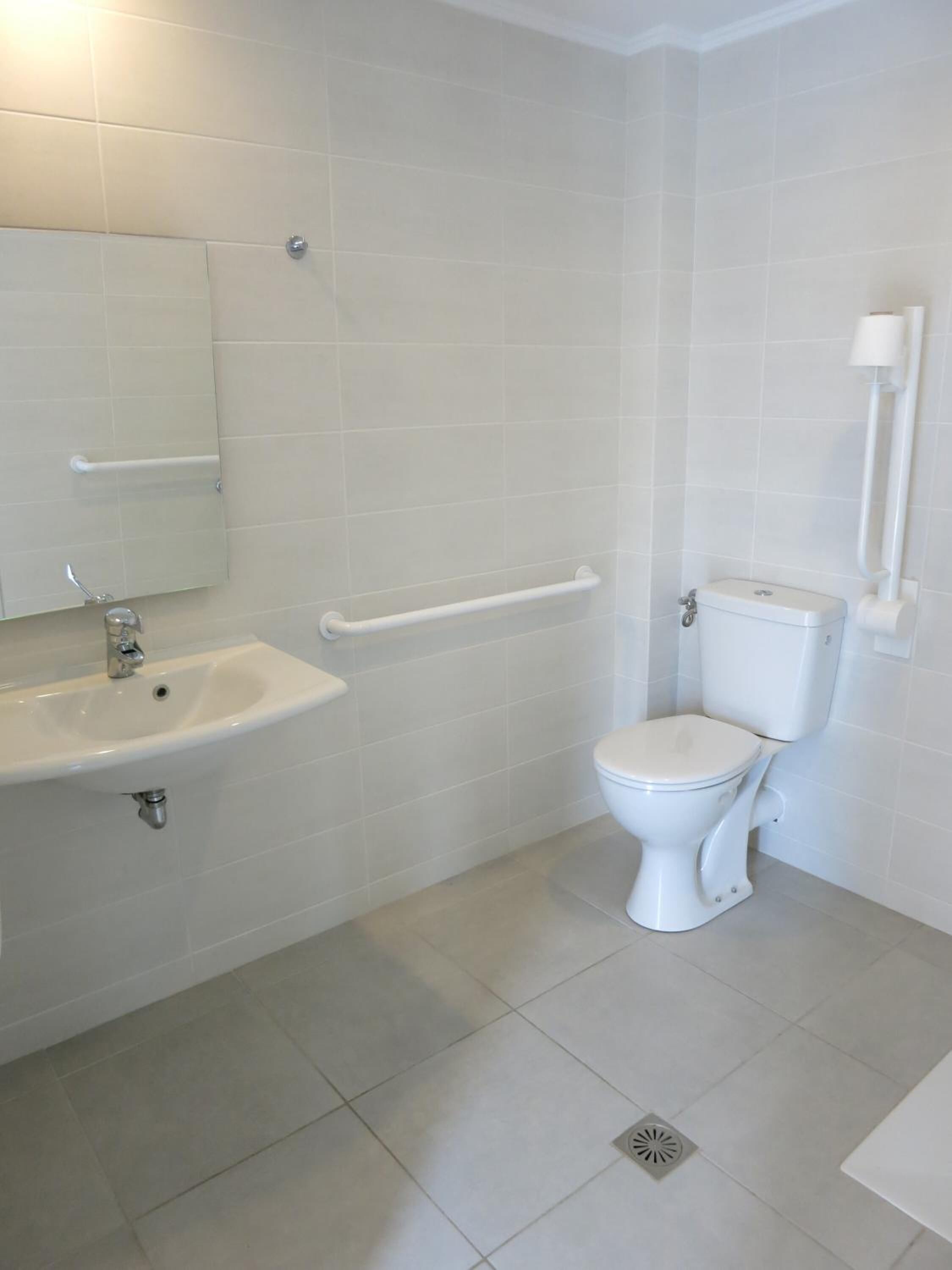 A bathroom with a white sink, mirror, toilet, and grab bars.