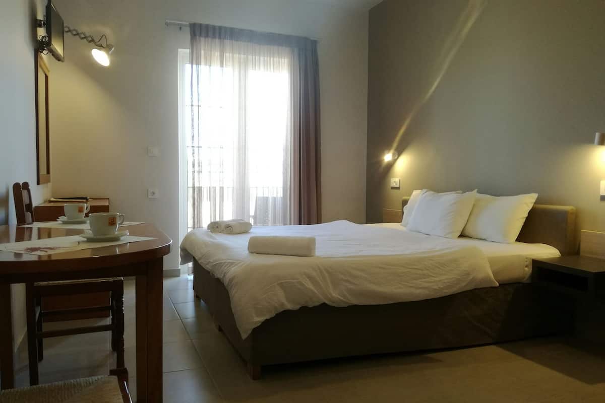Une chambre d’hôtel comprenant un lit, des tables de chevet, un bureau avec une chaise et une fenêtre avec des rideaux.