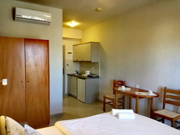 Habitación de hotel con cama, armario de madera, pequeña cocina y zona de comedor con mesa y sillas.