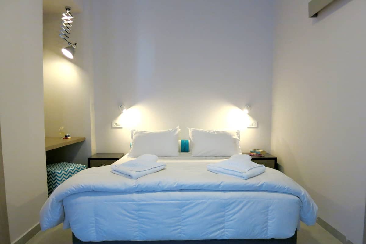 Un lit bien fait, avec du linge de lit blanc, deux lampes de chevet et une petite étagère contenant des articles de toilette.