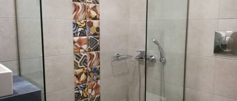 A shower area with a glass door, a tiled wall with a colorful pattern, and a toilet with a towel and a tissue box.