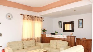 Una sala de estar con un sofá beige, una mesa de centro de madera, un reloj en la pared y un cabecero de madera.
