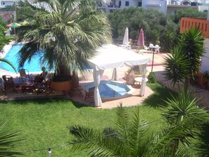 Ein Poolbereich mit Liegestühlen und Sonnenschirmen, umgeben von Palmen und einem weißen Pavillon.