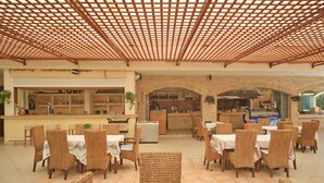 Un restaurante con sillas y mesas de mimbre, una zona de bar y una cocina visible a través de un arco.