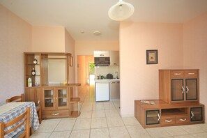 Eine kompakte Küche mit Kühlschrank, Herd und Spüle. Ein Holzschrank mit Glastüren und ein kleiner Esstisch mit Stühlen sind ebenfalls vorhanden.