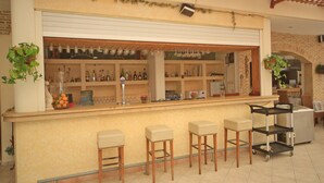 Una zona de bar con mostrador, taburetes, estantes con botellas y un refrigerador.