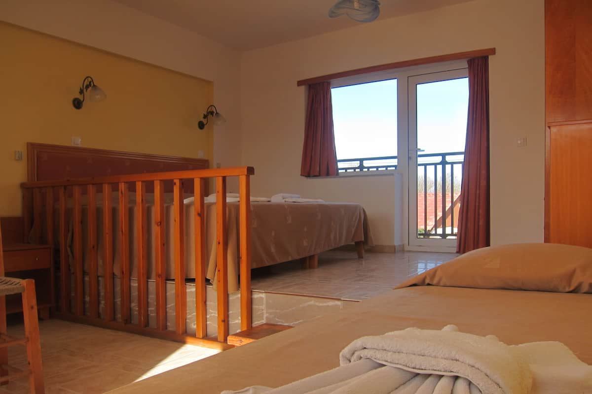 A hotel room with a bed, a desk, a chair, a balcony with curtains, and a view of the outside.