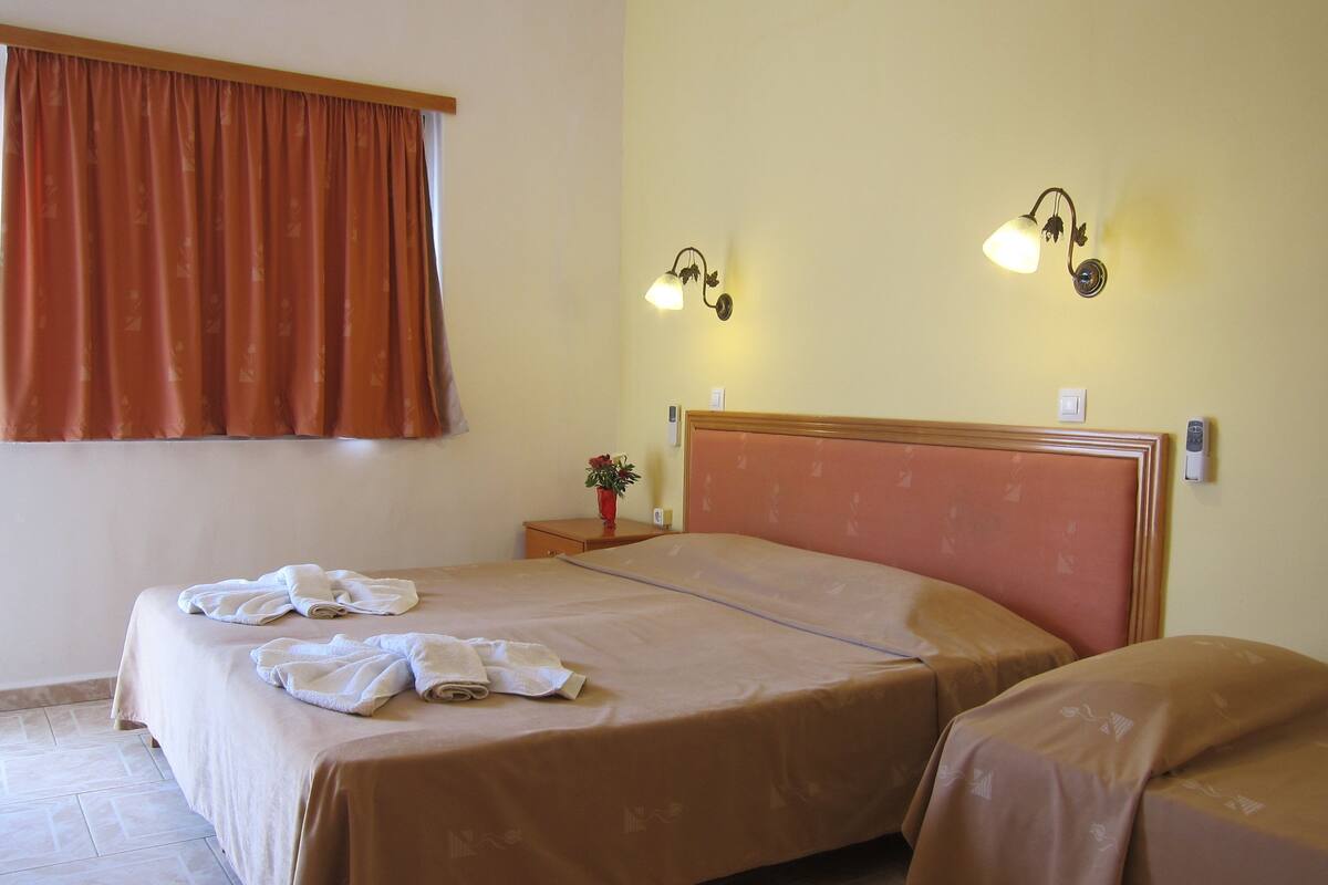 A hotel room with two beds, a nightstand, a vase with flowers, and wall-mounted lamps.