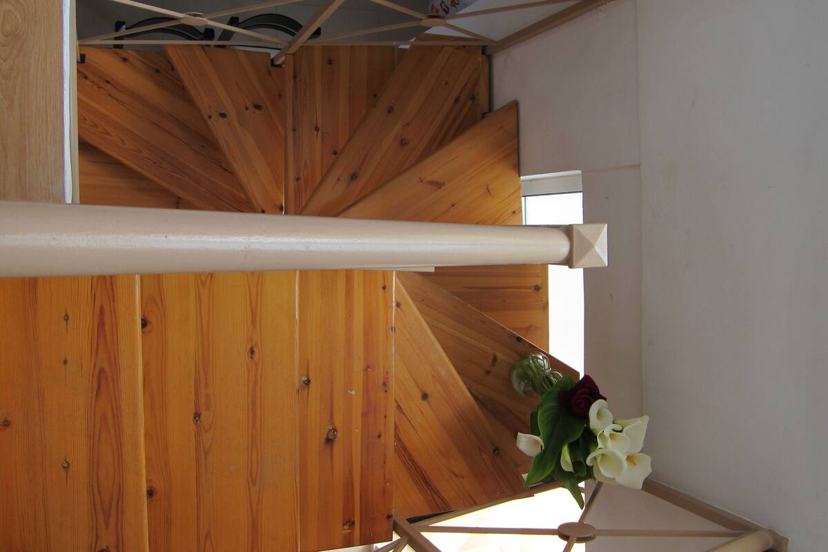 A wooden staircase with a white handrail and a flower arrangement at the top.