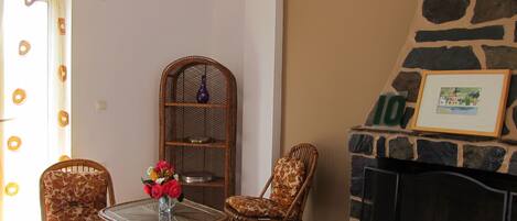 A living room with wicker furniture, a glass-top table with flowers, a stone fireplace, and a framed picture above it.