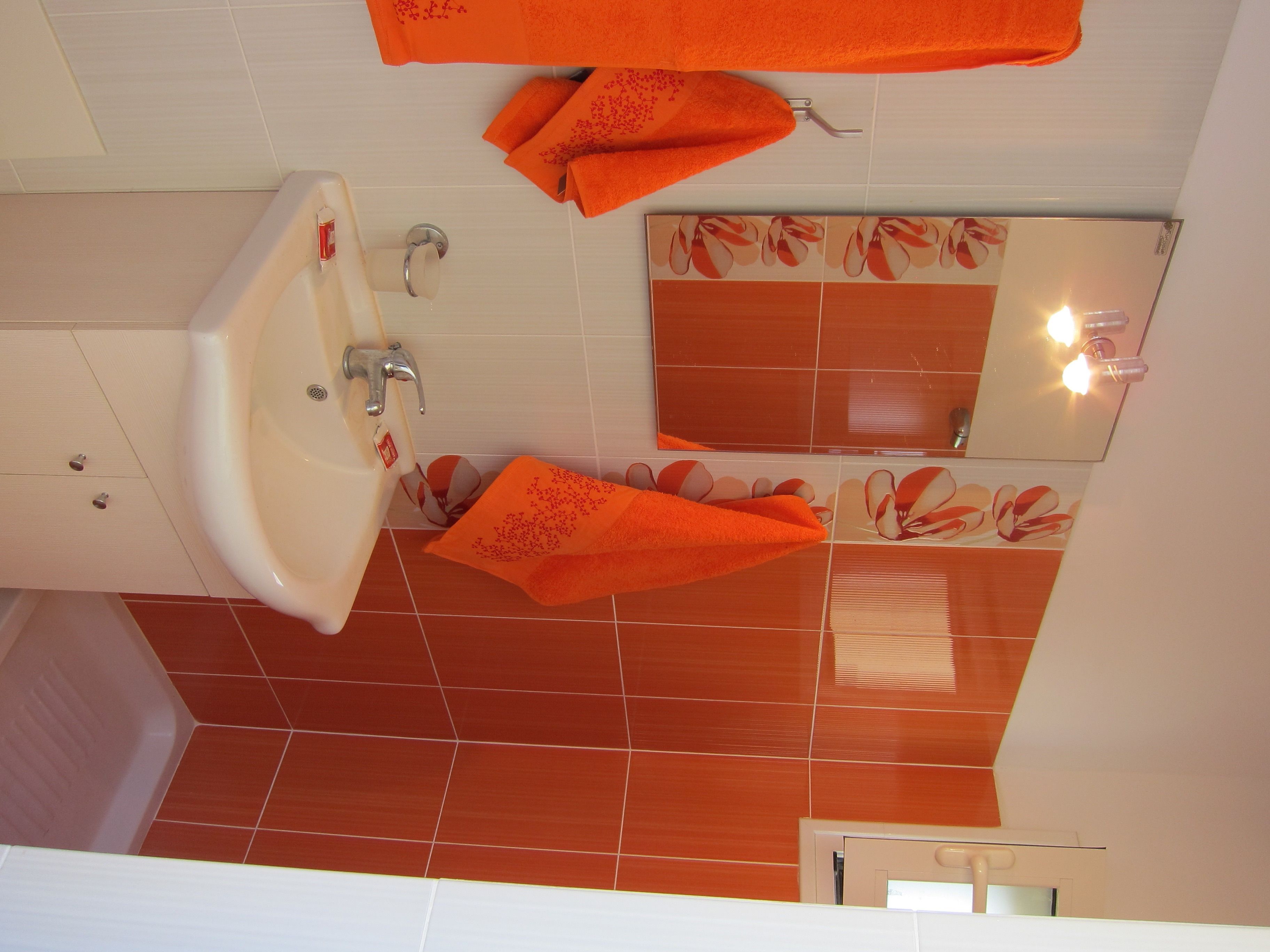 A bathroom with a sink, mirror, and orange towels.