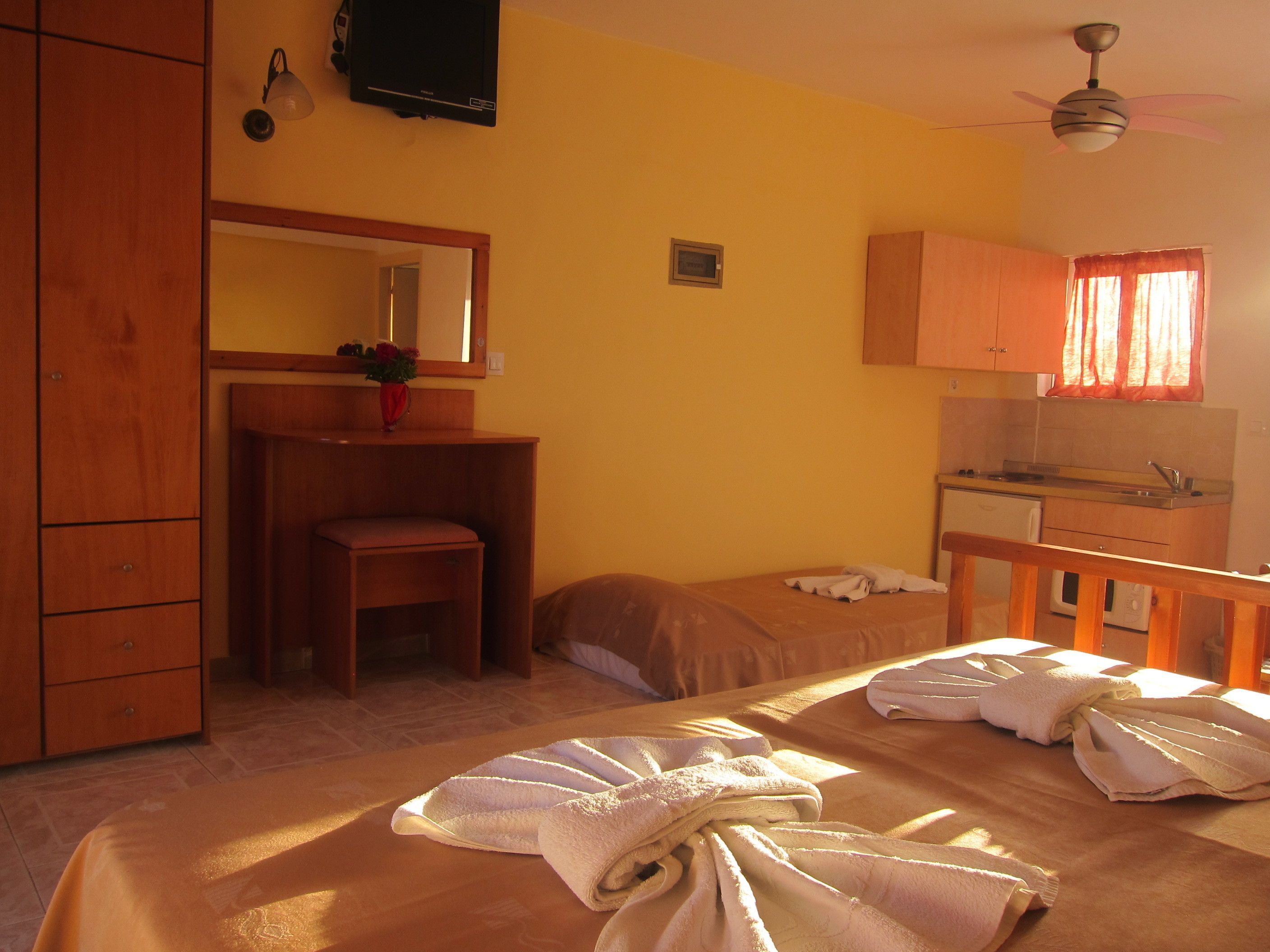 Un dormitorio con cama, escritorio, silla, espejo, ventilador de techo y ventana con cortinas.