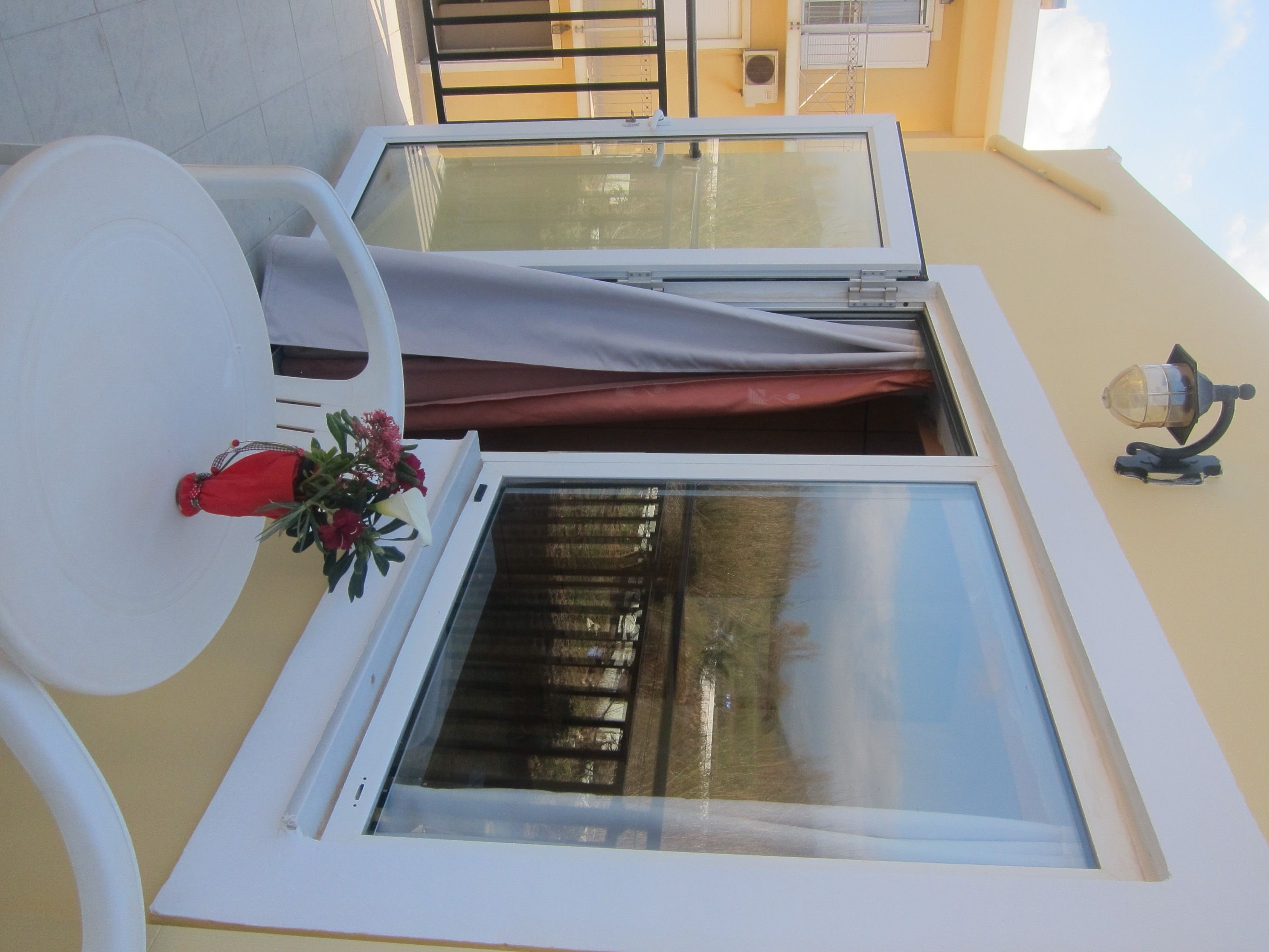 A room with a large window, a white chair, and a small table with a red decorative item.