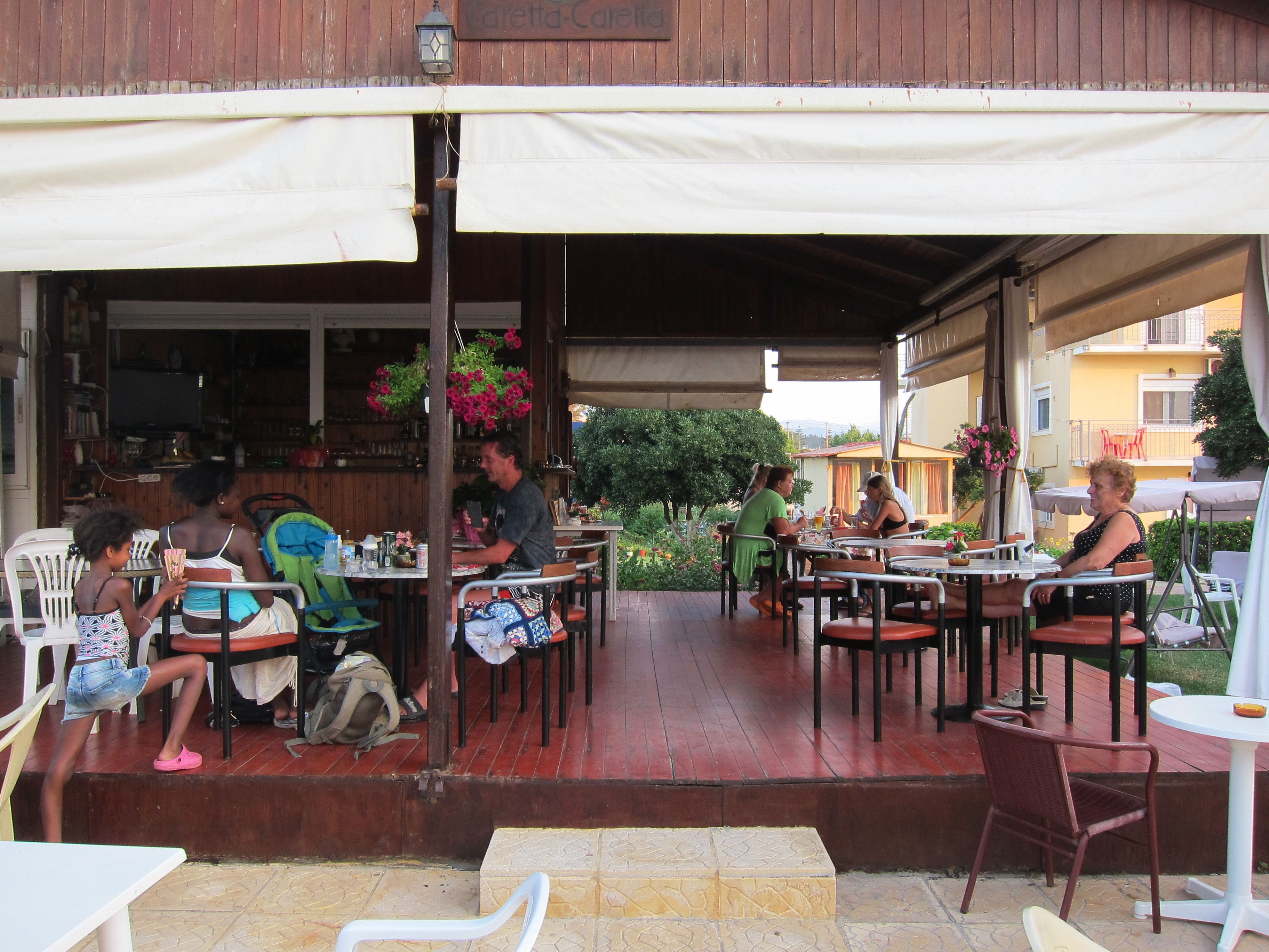 An outdoor café with tables and chairs, a wooden deck, and a covered area with a sign reading "Cafetta-Café".