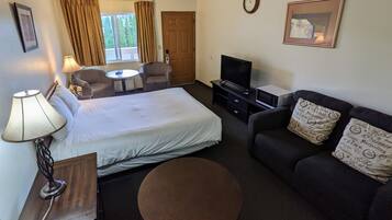 A hotel room with a bed, a sofa, a TV, a lamp, and a round table.